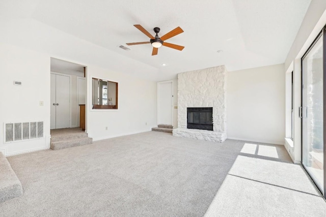 unfurnished living room with a stone fireplace, ceiling fan, and light colored carpet