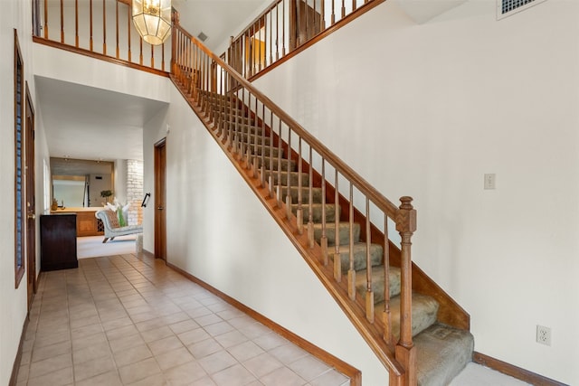 staircase with a notable chandelier, a high ceiling, and tile patterned floors