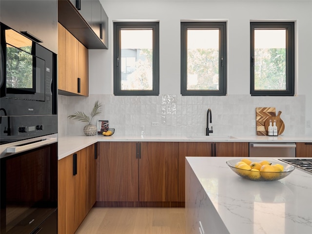 kitchen with sink, light hardwood / wood-style flooring, light stone countertops, appliances with stainless steel finishes, and tasteful backsplash