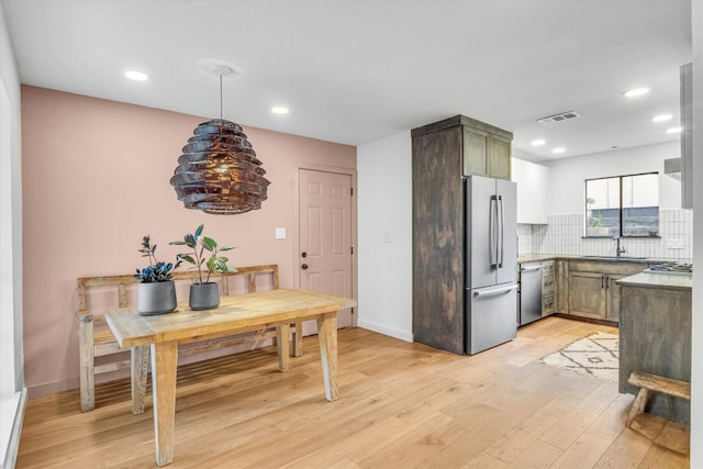 kitchen with sink, light hardwood / wood-style floors, stainless steel appliances, decorative light fixtures, and decorative backsplash