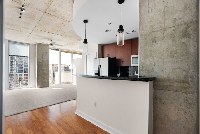 kitchen featuring stainless steel refrigerator with ice dispenser, kitchen peninsula, pendant lighting, hardwood / wood-style floors, and backsplash