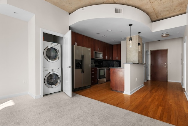 kitchen with stacked washer and clothes dryer, hanging light fixtures, dark brown cabinets, appliances with stainless steel finishes, and backsplash