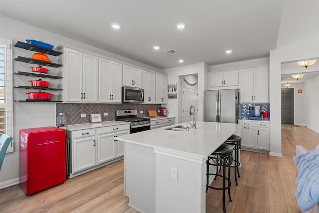 kitchen with a center island with sink, sink, appliances with stainless steel finishes, light hardwood / wood-style floors, and white cabinetry