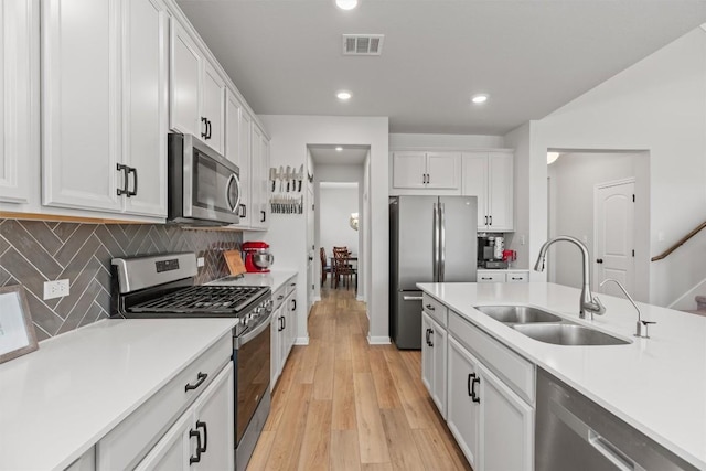 kitchen with white cabinetry, sink, stainless steel appliances, backsplash, and light wood-type flooring