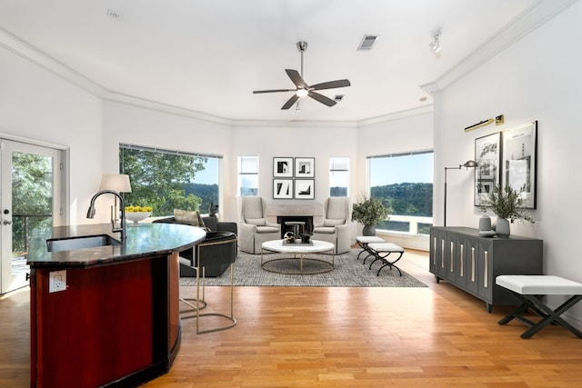 living area with light wood-style flooring, a fireplace, ornamental molding, and visible vents