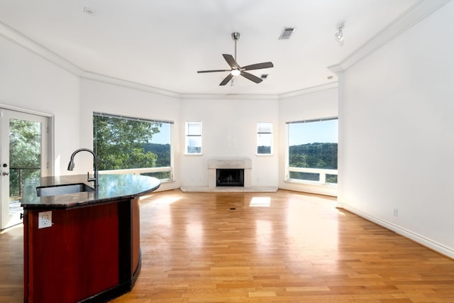 unfurnished living room featuring a fireplace with raised hearth, light wood-style flooring, a sink, baseboards, and crown molding