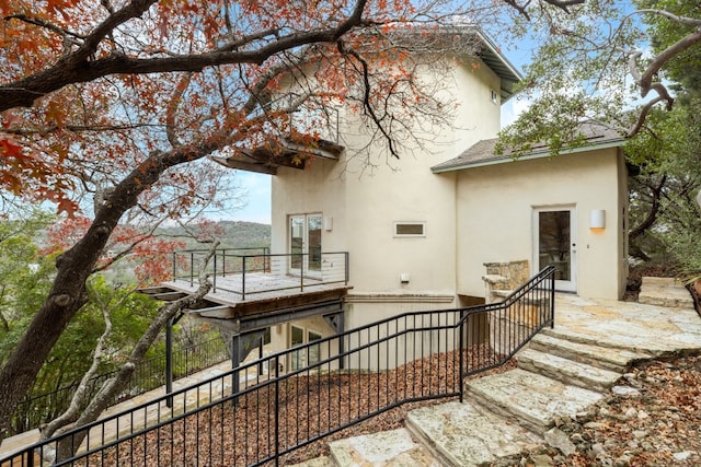 rear view of house featuring a balcony, fence, and stucco siding