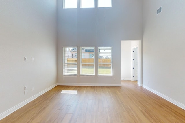 unfurnished room featuring a towering ceiling and light wood-type flooring