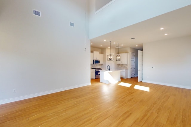 unfurnished living room featuring sink, light hardwood / wood-style floors, and a high ceiling