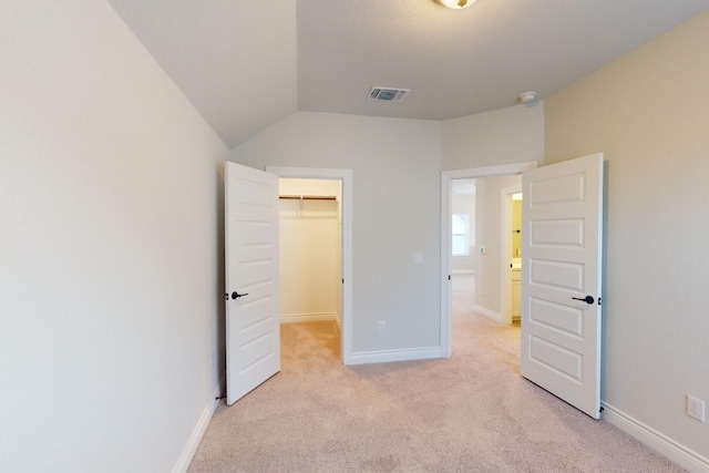 unfurnished bedroom with light carpet, a closet, a spacious closet, and lofted ceiling