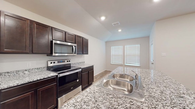 kitchen with dark brown cabinets, sink, vaulted ceiling, appliances with stainless steel finishes, and light stone countertops