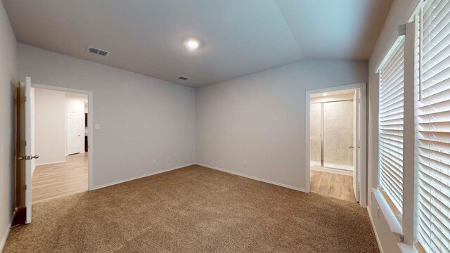 unfurnished bedroom with light carpet, connected bathroom, and vaulted ceiling