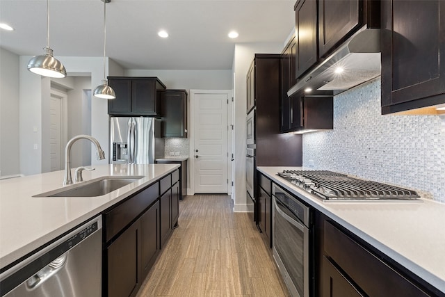 kitchen featuring pendant lighting, light hardwood / wood-style flooring, sink, backsplash, and appliances with stainless steel finishes