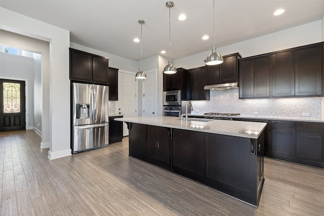 kitchen featuring light hardwood / wood-style flooring, a center island with sink, sink, stainless steel appliances, and hanging light fixtures