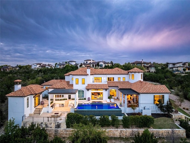 back of house at dusk featuring stucco siding, a tile roof, an outdoor hangout area, and a patio