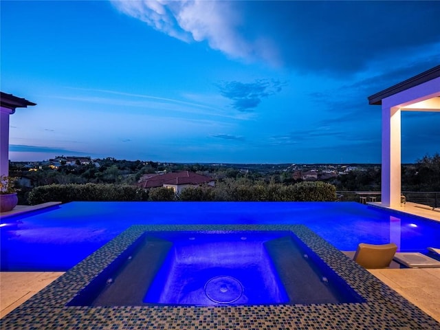 pool at dusk with a pool with connected hot tub