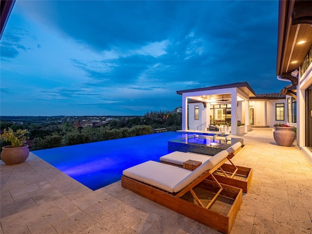 pool at dusk featuring a patio area and an in ground hot tub