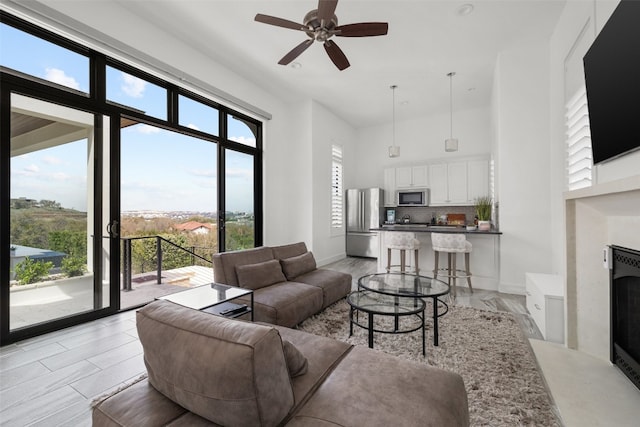 living room with ceiling fan, a high ceiling, baseboards, and a high end fireplace