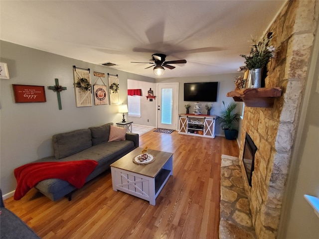 living room with a stone fireplace, hardwood / wood-style flooring, and ceiling fan