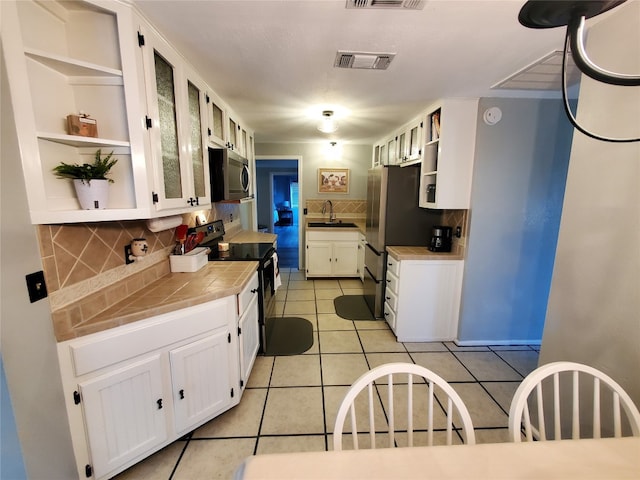 kitchen featuring stainless steel appliances, tile countertops, light tile patterned flooring, white cabinetry, and tasteful backsplash