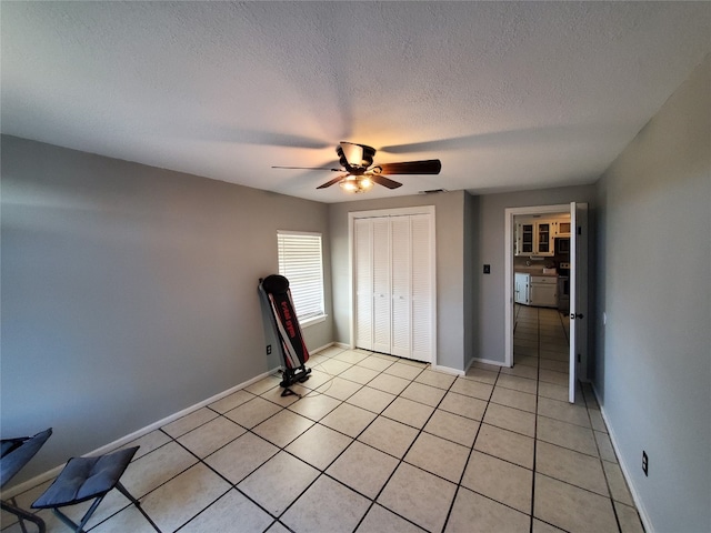 unfurnished bedroom with a textured ceiling, light tile patterned floors, ceiling fan, and a closet