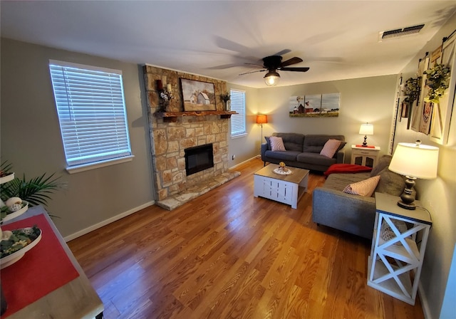 living room featuring hardwood / wood-style floors, a stone fireplace, and ceiling fan