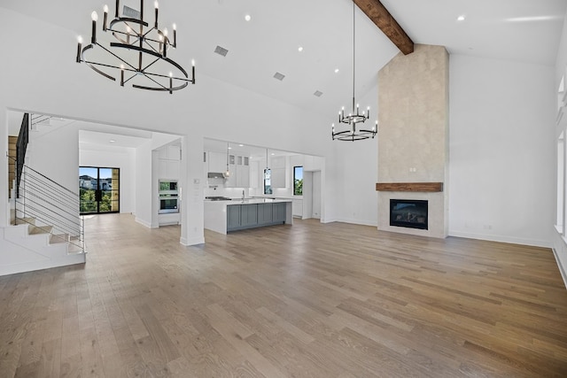 unfurnished living room featuring light hardwood / wood-style floors, high vaulted ceiling, a fireplace, beamed ceiling, and sink