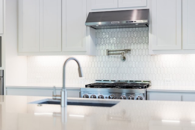 kitchen featuring backsplash, white cabinetry, sink, and wall chimney range hood