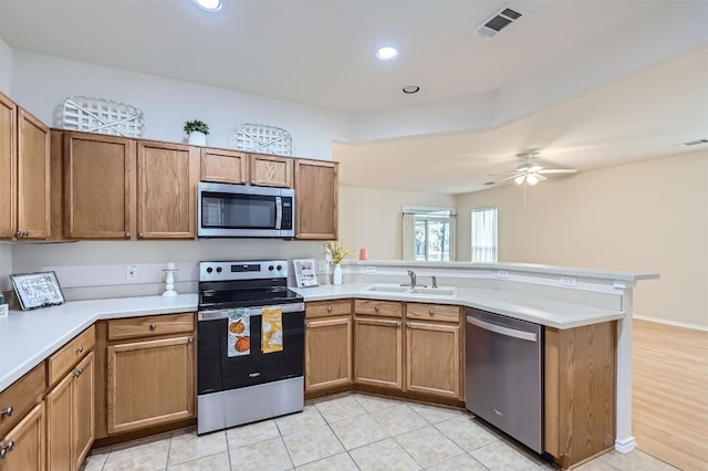 kitchen with kitchen peninsula, appliances with stainless steel finishes, ceiling fan, sink, and light hardwood / wood-style floors