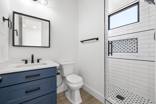 bathroom with hardwood / wood-style floors, tiled shower, vanity, and toilet