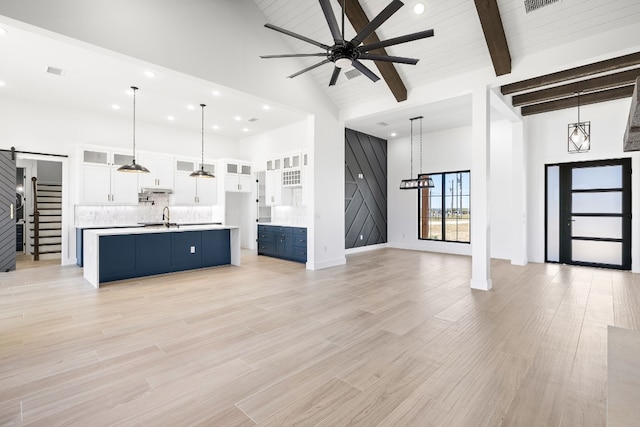 unfurnished living room featuring beamed ceiling, sink, light hardwood / wood-style flooring, high vaulted ceiling, and a barn door