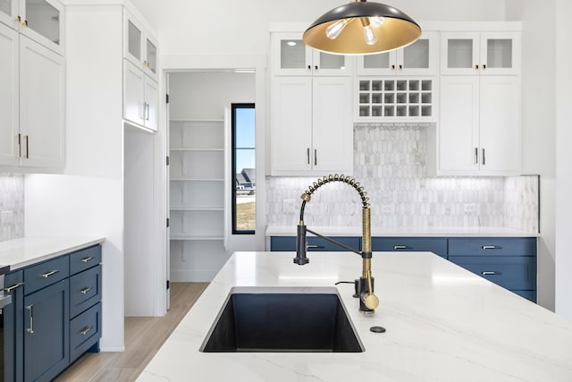 kitchen featuring blue cabinetry, white cabinets, light stone countertops, and sink