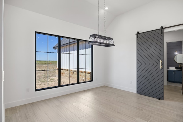 unfurnished dining area with a barn door, vaulted ceiling, and light hardwood / wood-style flooring