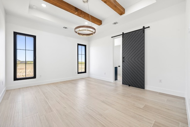 empty room featuring light hardwood / wood-style floors, beamed ceiling, and a barn door