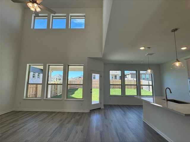 unfurnished living room featuring ceiling fan, plenty of natural light, dark wood-type flooring, and sink