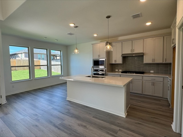 kitchen with a center island with sink, dark wood-type flooring, and appliances with stainless steel finishes