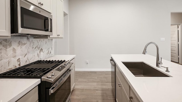 kitchen with stainless steel appliances, a sink, light wood-style floors, light countertops, and decorative backsplash