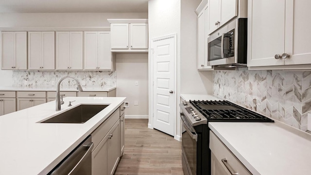 kitchen featuring stainless steel appliances, a sink, light countertops, and light wood-style floors