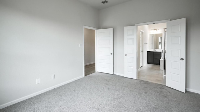 unfurnished bedroom featuring baseboards, ensuite bathroom, and light colored carpet