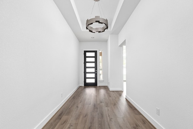 doorway featuring a tray ceiling, hardwood / wood-style flooring, and an inviting chandelier