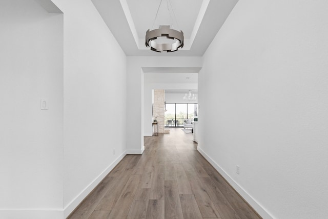 corridor with a tray ceiling, light hardwood / wood-style floors, and an inviting chandelier