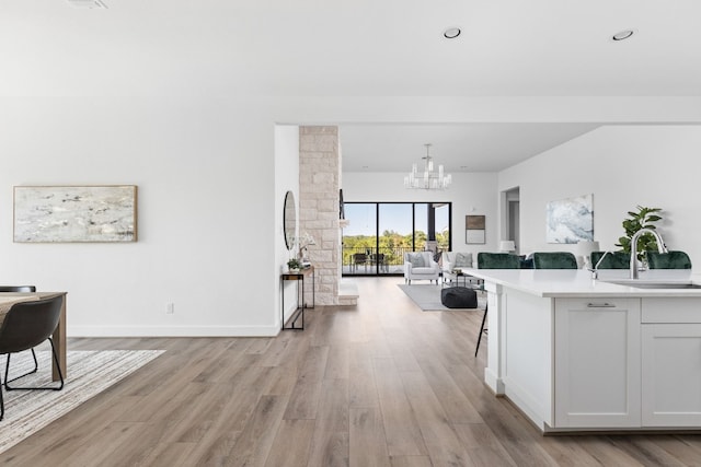 kitchen featuring sink, hanging light fixtures, a notable chandelier, light hardwood / wood-style floors, and white cabinetry