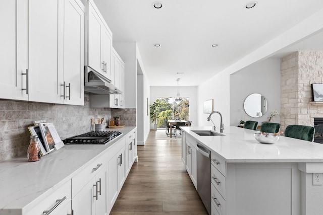 kitchen with appliances with stainless steel finishes, light stone counters, a kitchen island with sink, sink, and white cabinetry