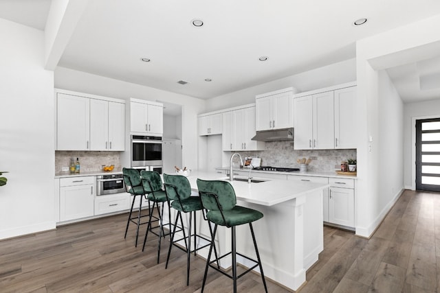 kitchen featuring a kitchen bar, appliances with stainless steel finishes, sink, a center island with sink, and white cabinetry