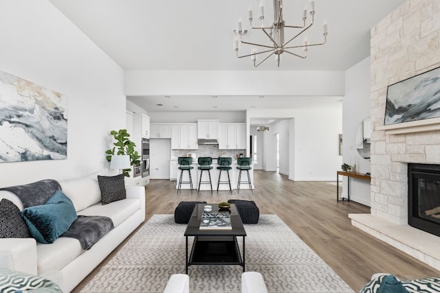 living room with a stone fireplace, hardwood / wood-style floors, and an inviting chandelier