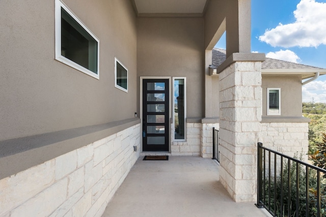 entrance to property with a shingled roof, stone siding, and stucco siding