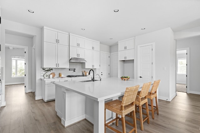 kitchen featuring white cabinets, sink, light wood-type flooring, and an island with sink