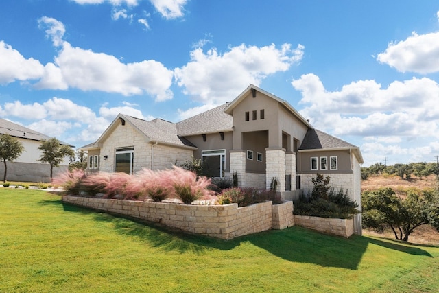 exterior space featuring a shingled roof, stucco siding, a front yard, and stone siding