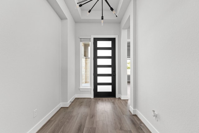 foyer entrance with baseboards, wood finished floors, and a chandelier