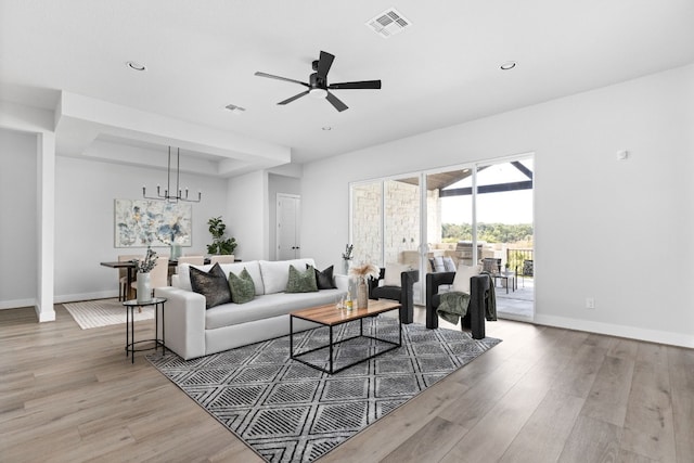 living room with light hardwood / wood-style floors and ceiling fan with notable chandelier